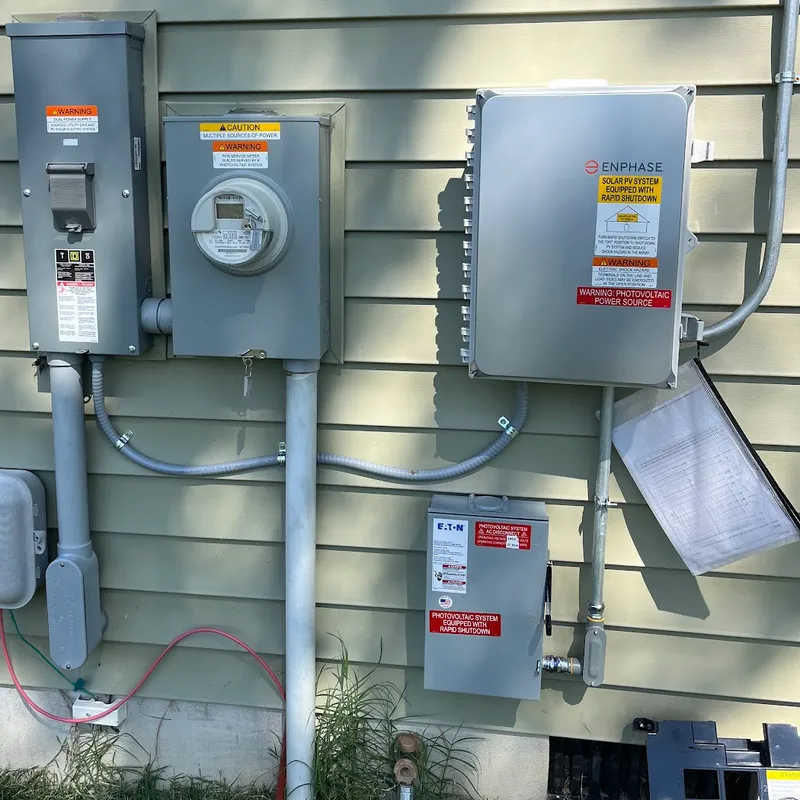 Solar electrical equipment on the side of a house: utility disconnect, electric meter, Enphase IQ Combiner at top right, and the PV system AC disconnect at bottom right