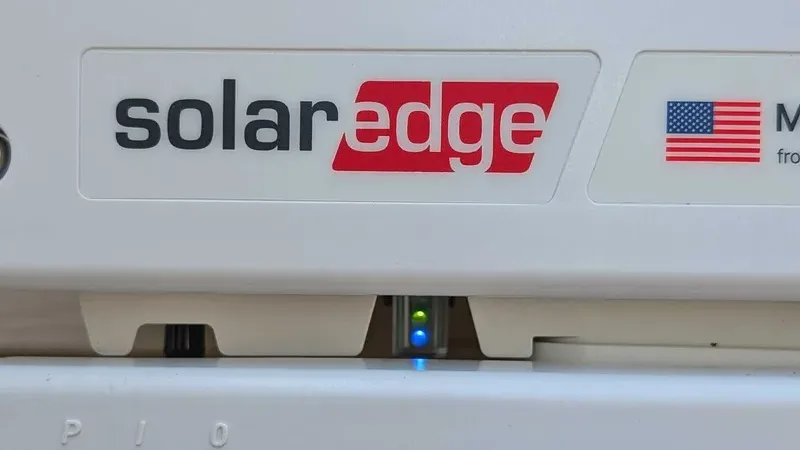 SolarEdge inverter with the green production and blue monitoring LEDs lit below the SolarEdge logo